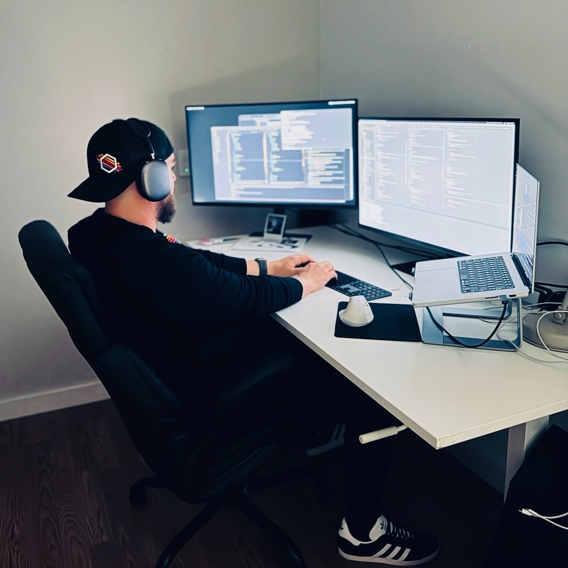 A photo of Sean sitting at his desk, upon which are an open notebook computer and two external displays.